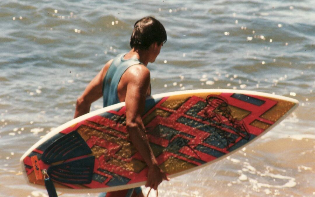 Male surfer walking up the beach with a fluro board.